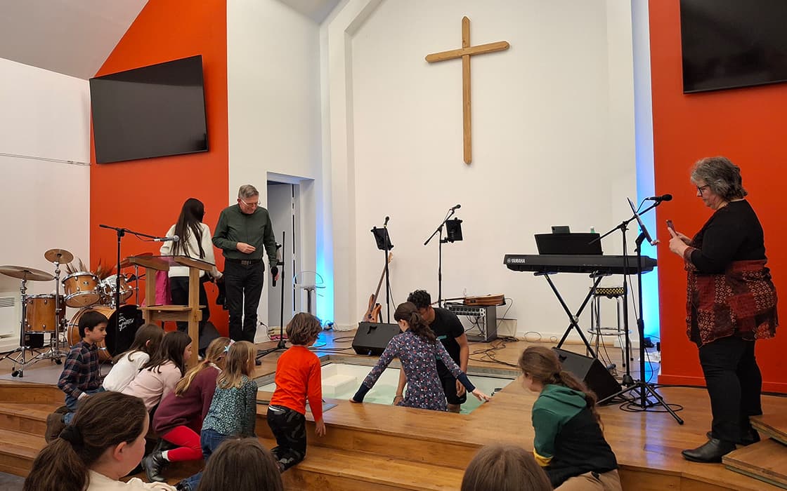 Kinder und Erwachsene versammeln sich zur Taufe auf einer Kirchenbühne, die Gemeindegründungen in Westfrankreich widerspiegelt.