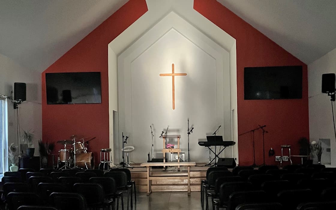Innenraum einer Kirche in Ostfrankreich mit Bühne, Instrumenten, großem Kreuz und Reihen von leeren Stühlen für Gemeindegründungen.