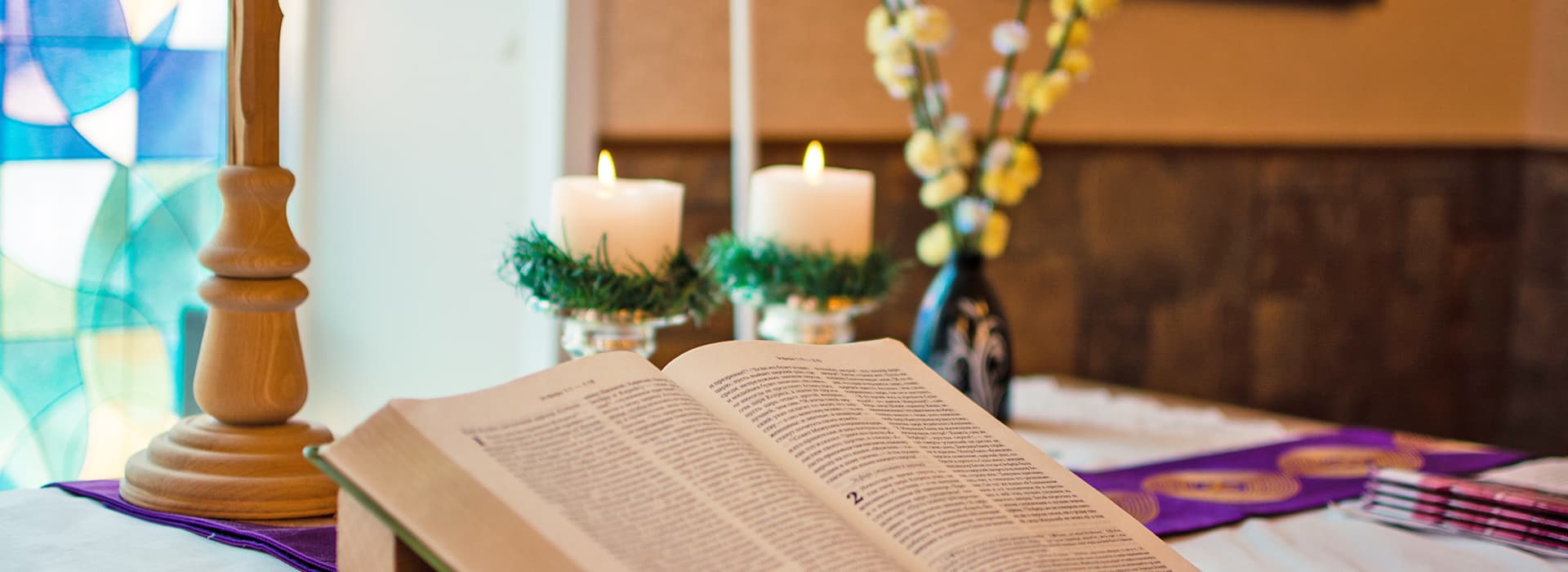 Eine aufgeschlagene Bibel auf einem geschmückten Tisch - mit Kerzen, Blumen und Glasmalerei - erinnert an TEE in Russland.