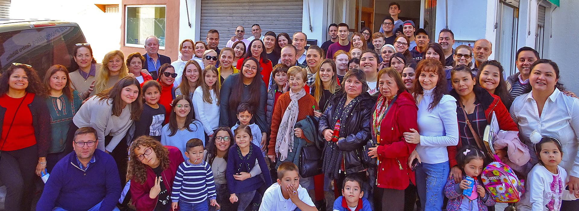 Eine große Gruppe aller Altersgruppen lächelt vor einem Gebäude in Spanien, das an einem sonnigen Tag zur Gemeindearbeit versammelt ist.