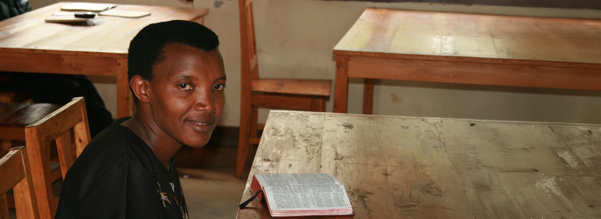 Eine Person sitzt an einem Holztisch in einem Klassenzimmer des TEE Burundi und absolviert ihre theologische Ausbildung.