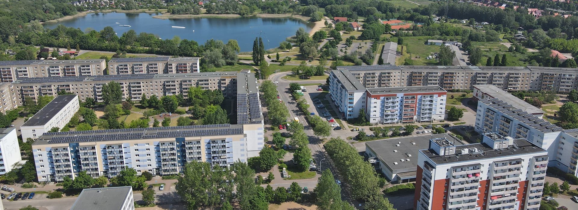 Luftaufnahme der Wohnhäuser der Oase Neubrandenburg in Deutschland, umgeben von Bäumen, einem See und üppiger Vegetation.