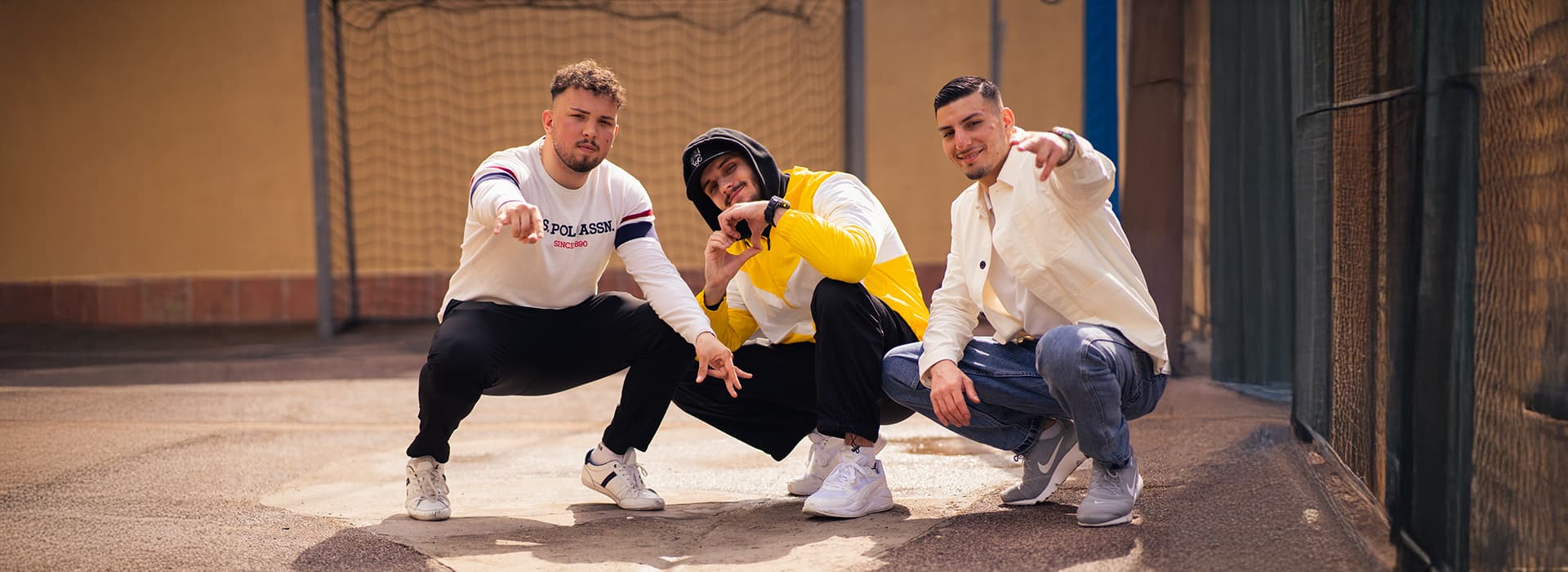 Drei junge Männer posieren selbstbewusst in lässiger Streetwear im Freien und lassen Lubu Beatz-Vibes in die Kamera strahlen.