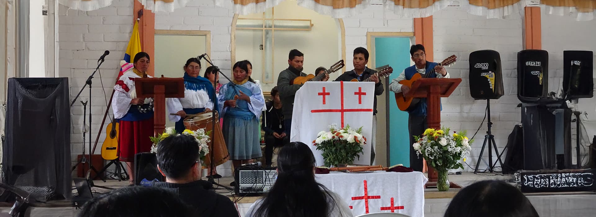 Eine Gruppe von Musikern und Sängern tritt mit Instrumenten und Blumenschmuck auf einer Kirchenbühne in Ecuador auf.