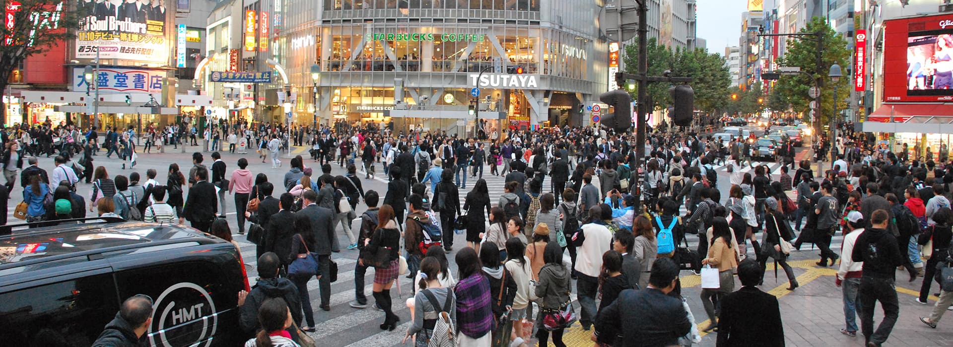 Menschenmengen überqueren eine belebte Kreuzung im pulsierenden Japan, umgeben von hellen Lichtern und Schaufenstern.
