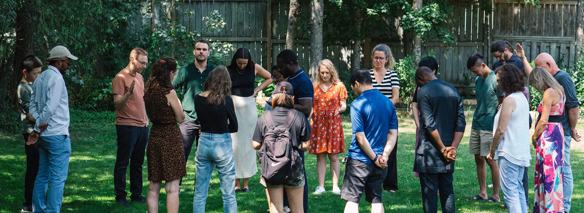 Eine bunt gemischte Gruppe steht im Freien im Kreis, die Köpfe zum Gebet gesenkt, und denkt gemeinsam in der Reach Community Church in Kanada nach.