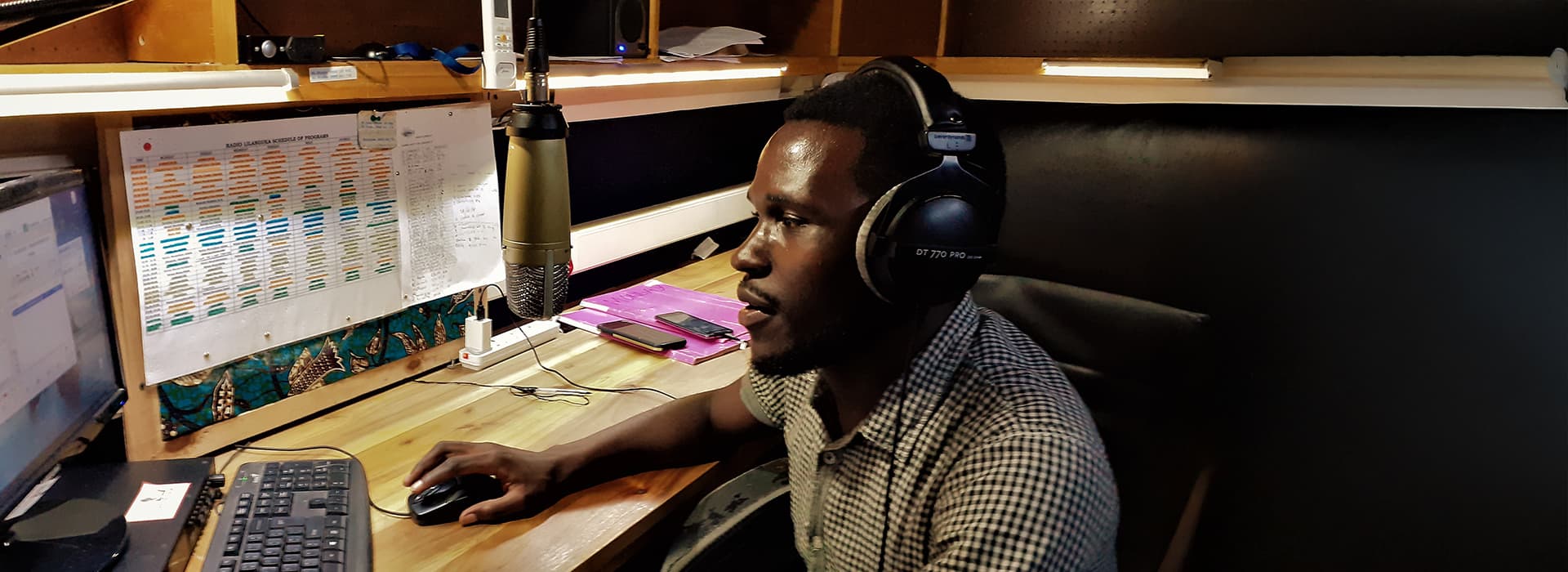 Ein Mann mit Kopfhörern spricht im Studio von Radio L in Malawi in ein Mikrofon und benutzt einen Computer an seinem Schreibtisch.