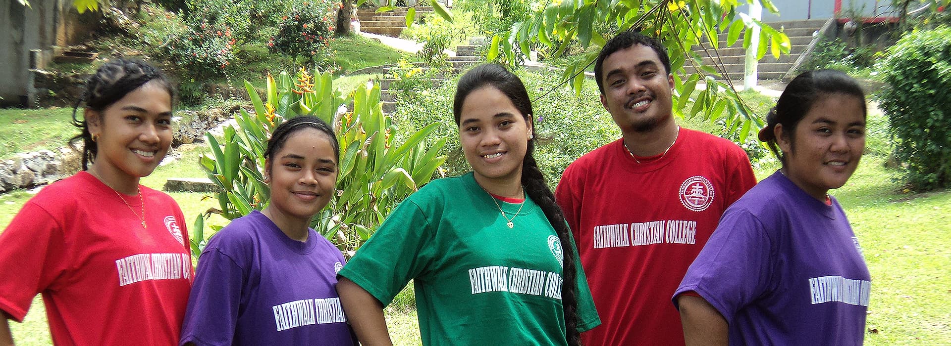 Fünf Menschen in farbenfrohen Hemden stehen lächelnd im Freien der Pacific Islands University, hinter ihnen das Grün der Mikronesien.