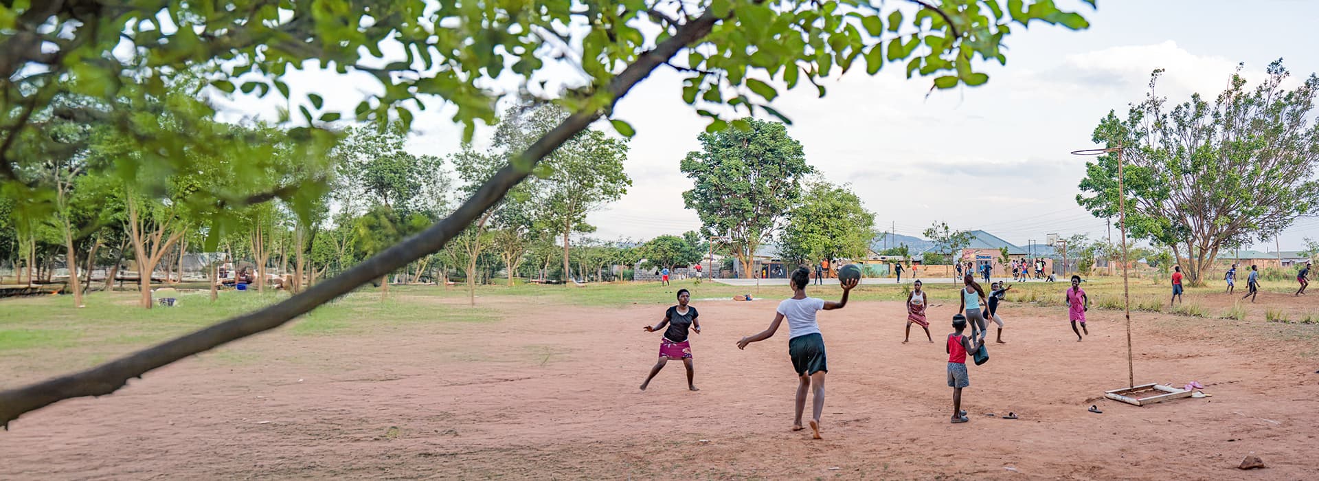 Kinder spielen auf einem großen, offenen Feld in Mushili, Sambia, mit Sportgeräten von Hilfe zum Leben unter einem teilweise bewölkten Himmel.