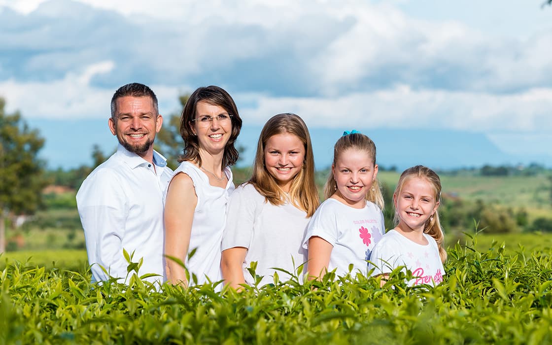 Eine lächelnde fünfköpfige Familie, darunter Mirjam Berger und Joachim Berger, posiert auf einer grünen Wiese unter einem blauen Himmel mit Wolken.