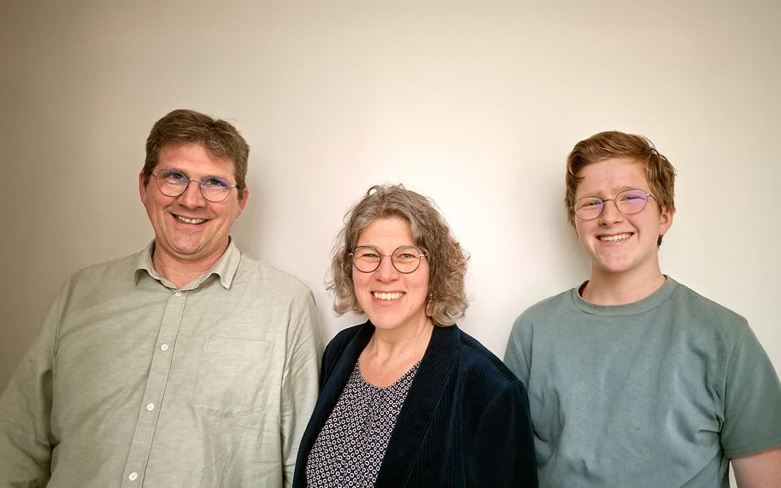 Michael Eckstein, Tina Eckstein und eine weitere Person lächeln in die Kamera und stehen vor einer hellen Wand.