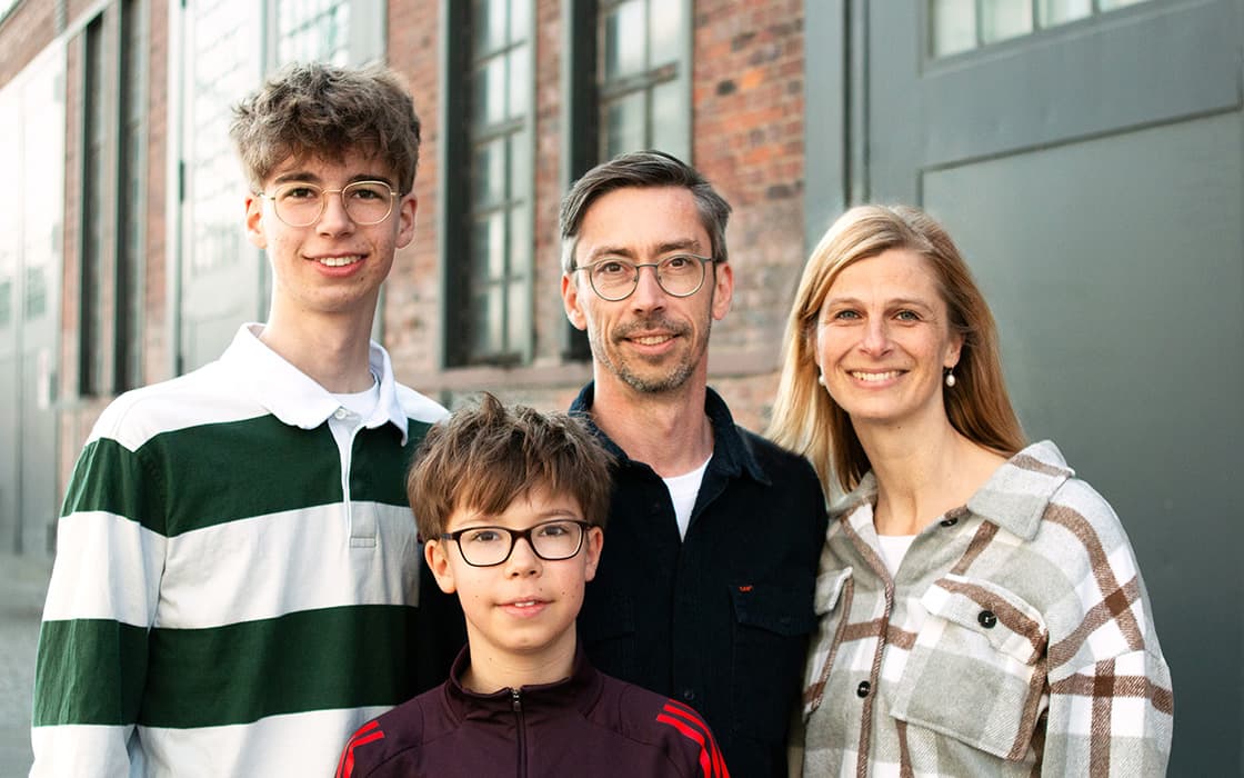 Angelika Farr und Dirk Farr mit ihren beiden Jungen, die im Freien in der Nähe eines Backsteingebäudes lächeln.