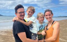 Eine lächelnde vierköpfige Familie, darunter Manuel Feige und Christina Feige, steht gemeinsam an einem Sandstrand mit blauem Himmel und Meer.
