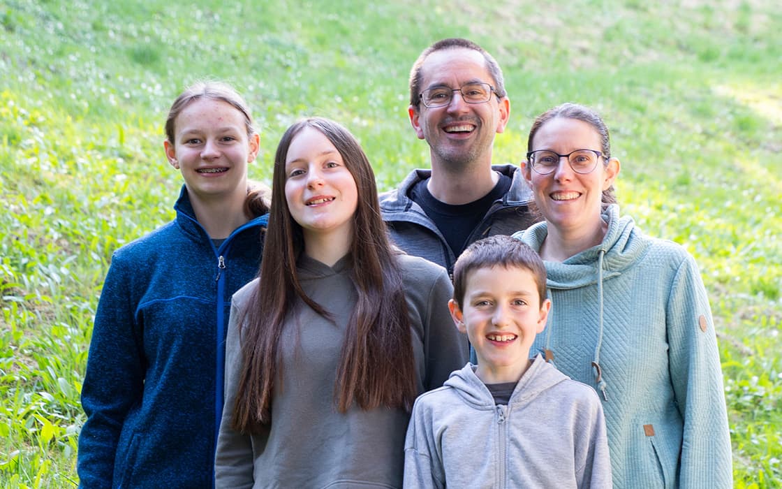Eine lächelnde fünfköpfige Familie, darunter Ben Geiss und Yvonne Geiss, steht im Freien im Gras und posiert für ein Foto.