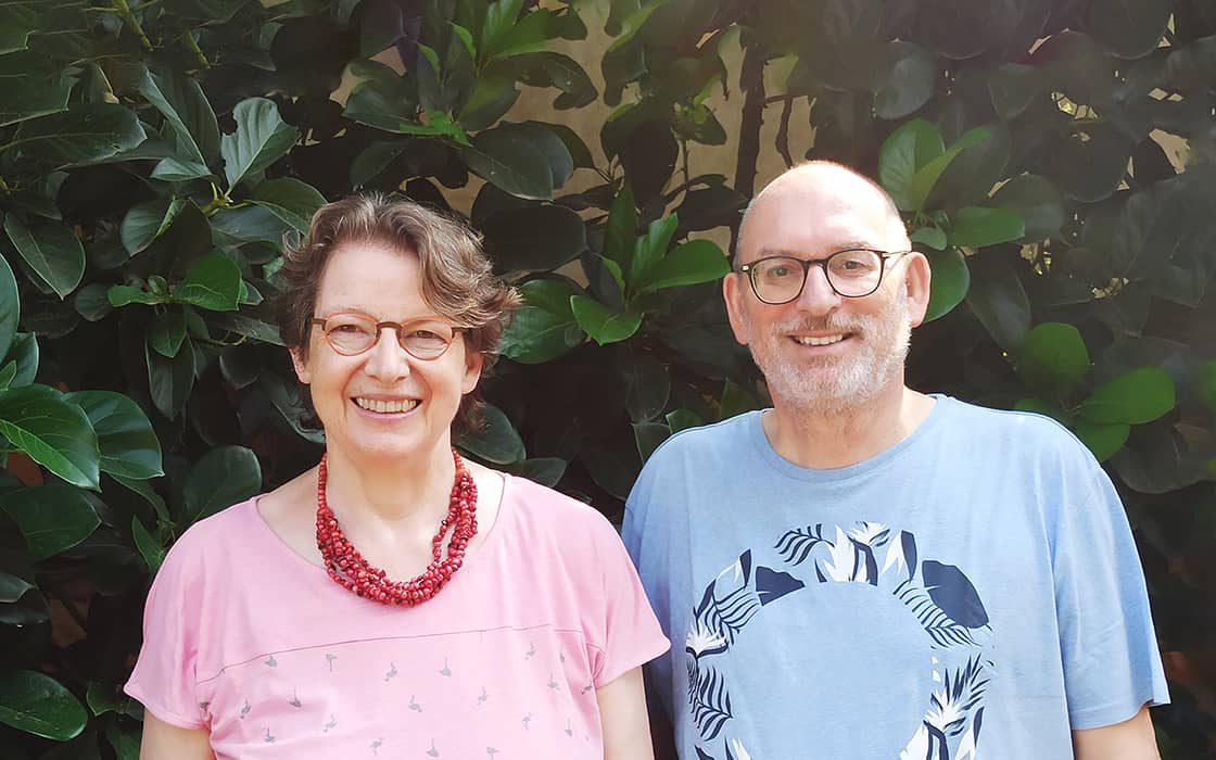 Albrecht Hengerer und Annegret Hengerer lächeln vor einem grünen Gebüsch, sie tragen rosa und hellblaue Hemden.
