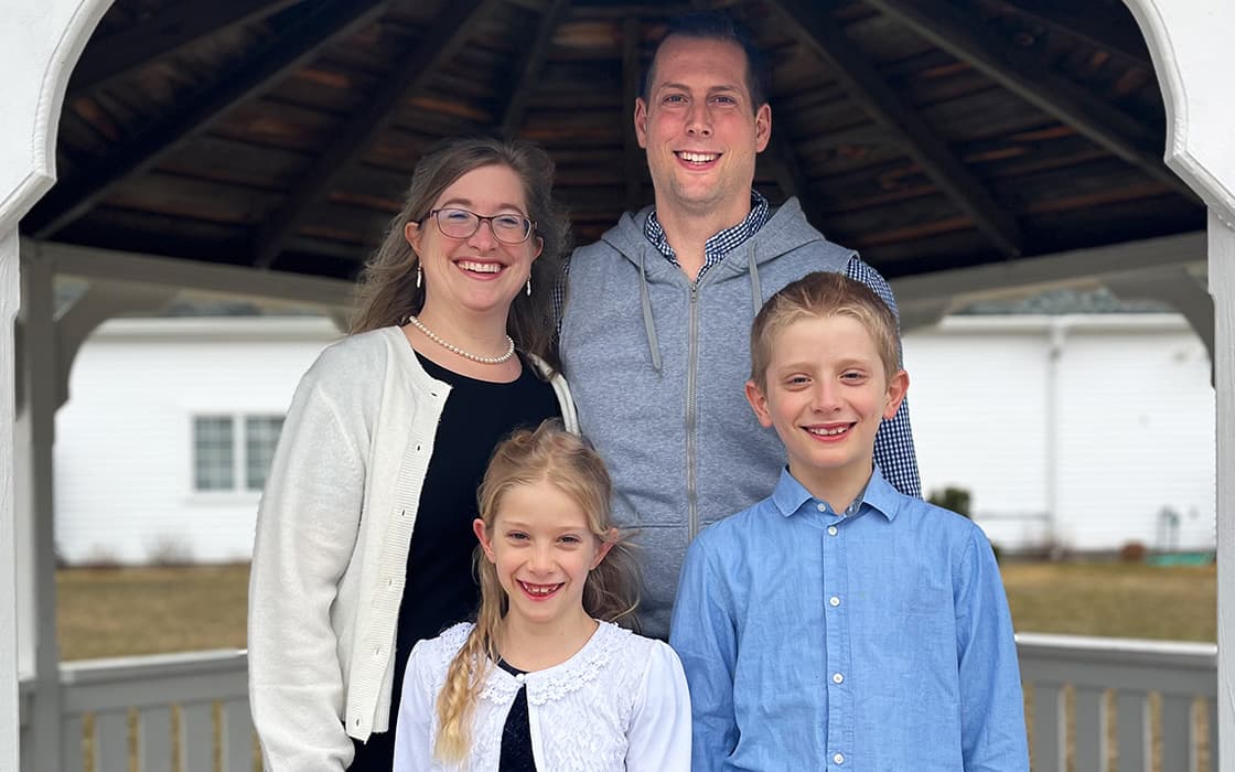 Sarah Müller und Tobias Müller lächeln mit ihrer Familie in einem Pavillon, ein weißes Haus im Hintergrund.