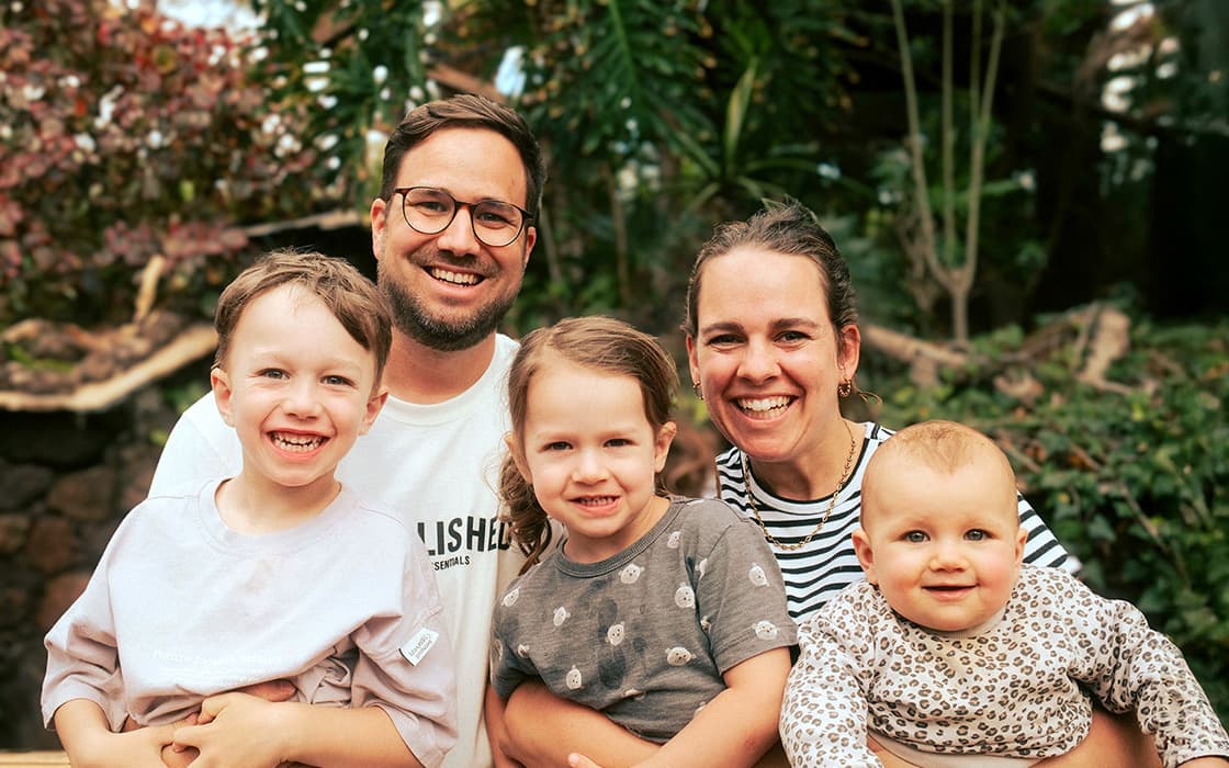 Eine lächelnde Familie, zu der auch Cathrin Pfrommer und Sebastian Pfrommer gehören, posiert im Freien in einer üppigen, grünen Umgebung.