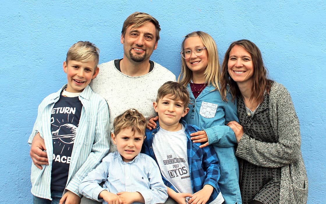 Eine lächelnde fünfköpfige Familie - Daniel Suchalla, Rosita Suchalla und ihre drei Kinder - posiert vor einer strahlend blauen Wand.