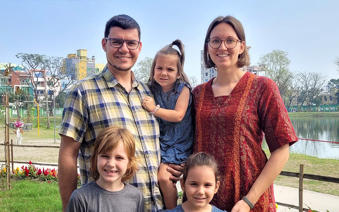 Eine lächelnde fünfköpfige Familie, darunter Verena Tschauner, posiert im Freien in der Nähe eines Sees mit Gebäuden und Bäumen im Hintergrund.