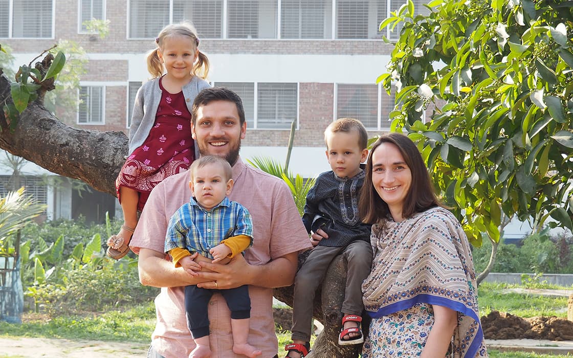 Eine lächelnde fünfköpfige Familie, darunter Micha Ulmer, posiert im Freien in der Nähe eines Baumes mit einem Gebäude im Hintergrund.