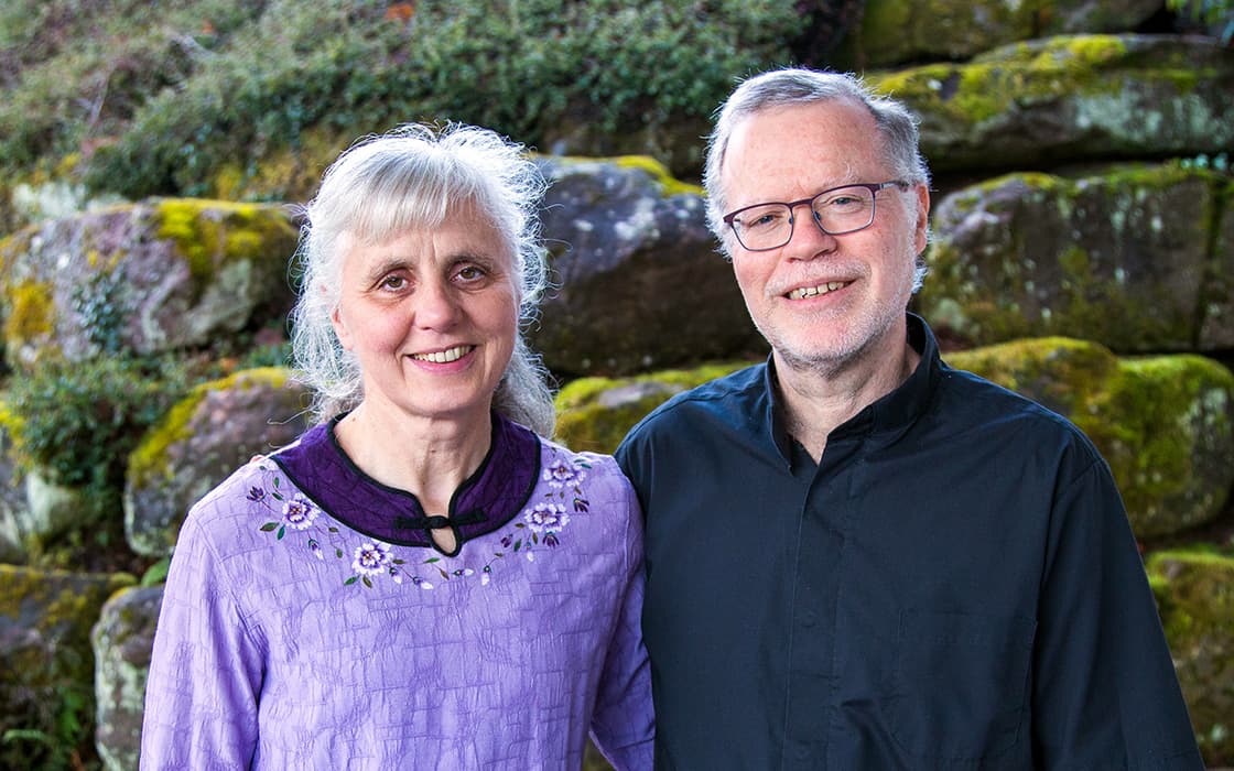 Erika Volz in lila Bluse und Klaus-Dieter Volz in Schwarz lächeln sich im Freien an moosbewachsenen Steinstufen an.