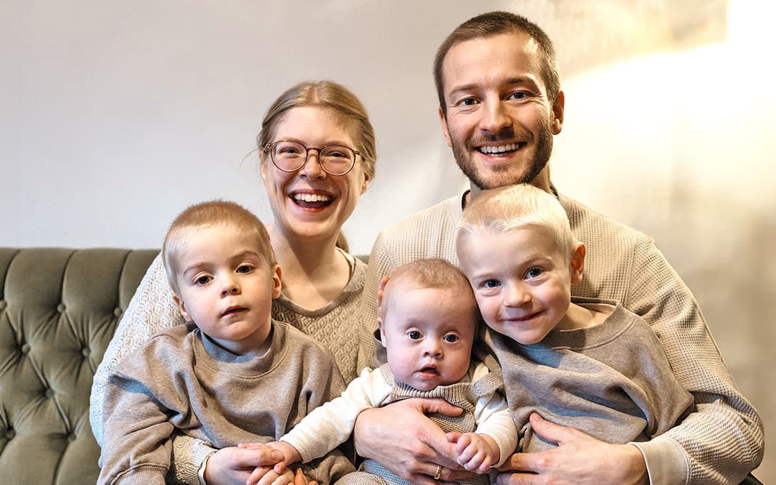 Ein lächelndes Ehepaar, Herrmann und Jael Stamm, sitzt mit drei Kindern in neutraler Kleidung auf einer Couch.