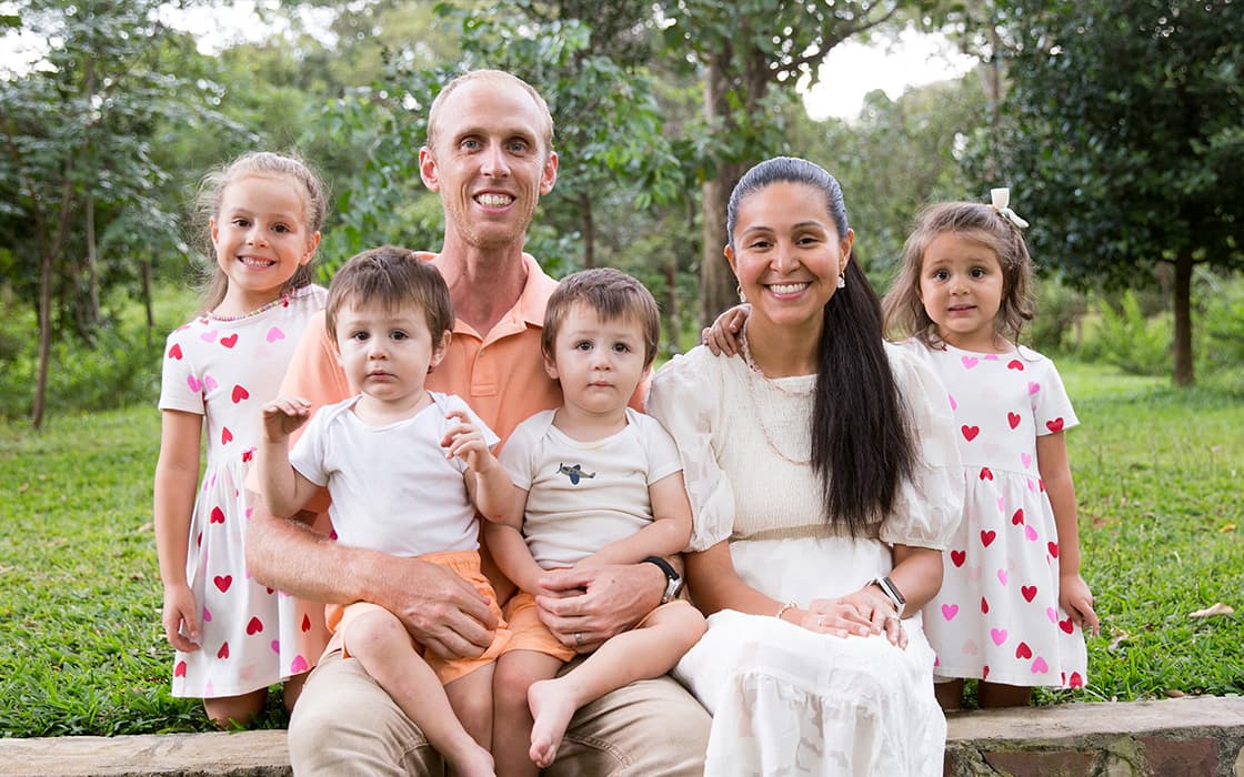 Jovita Pflaum und Martin Pflaum mit ihren vier kleinen Kindern lächeln gemeinsam in einem grünen Park.
