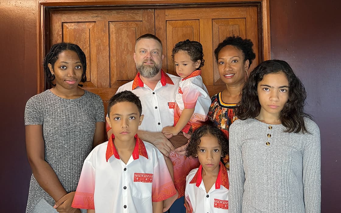 Stephanie Poriz und Jesse Poriz stehen mit ihrer siebenköpfigen Familie im Haus, ohne zu lächeln, vor einer Holztür.