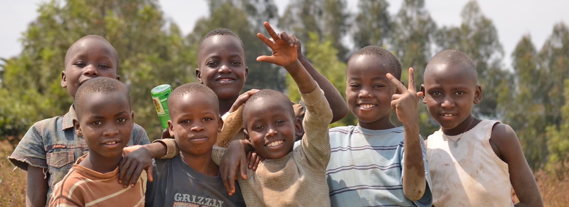 Sieben lächelnde Kinder, darunter Esther Stoll und Manuel Stoll, stehen im Freien dicht beieinander und winken in die Kamera.