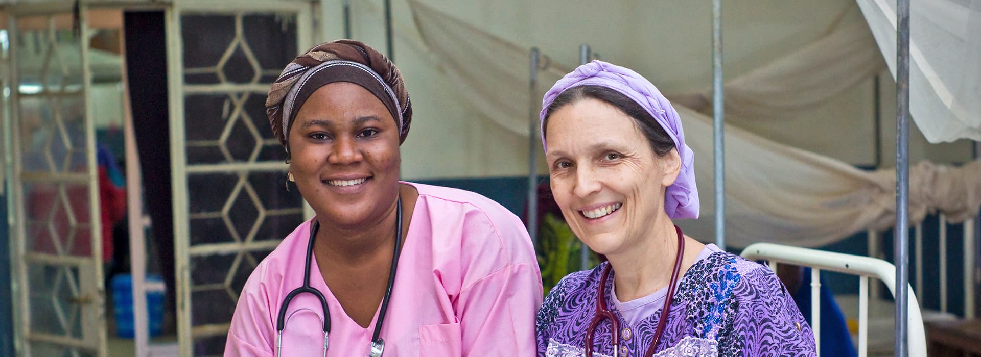 Zwei Mitarbeiterinnen des Gesundheitswesens mit Kopftüchern und Kitteln lächeln in der medizinischen Klinik von Dr. Esther Pflaum.