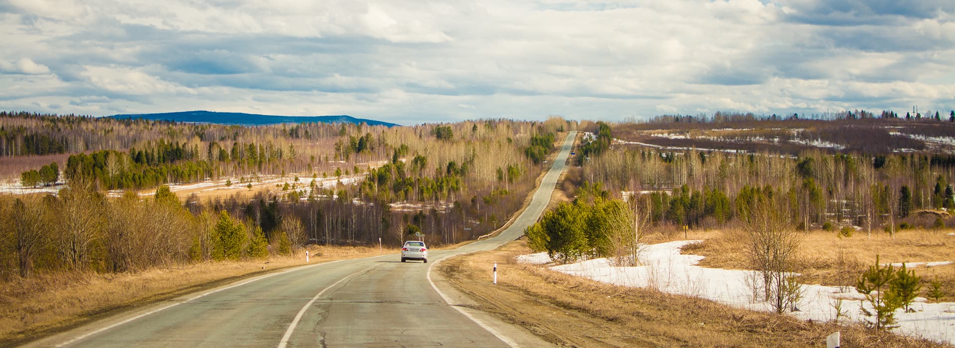 Ein Auto fährt eine kurvenreiche Landstraße hinunter, während der Himmel wolkenverhangen ist, was an eine Szene aus Olga Lies oder Waldemars Erzählungen erinnert.