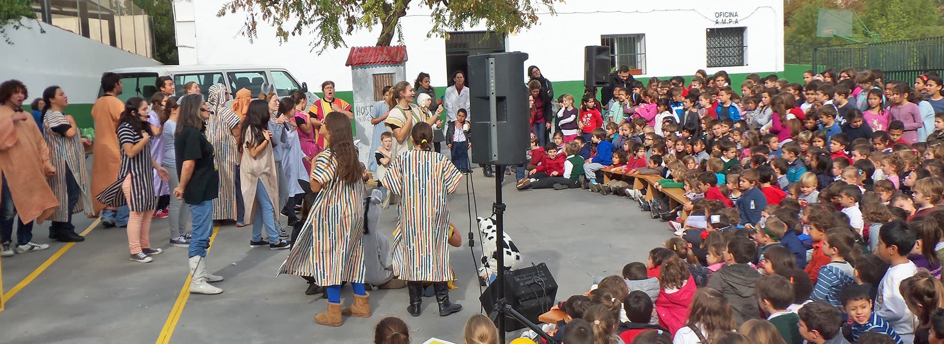 Kinder schauen Carolin Hertler und Theo Hertler zu, wie sie in ihren Kostümen vor der Schule auftreten, während viele Menschen an der Veranstaltung teilnehmen.