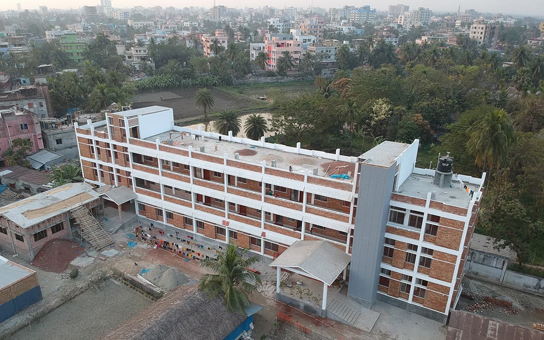 Ein dreistöckiges Schulgebäude aus Backstein, umgeben von Bäumen, mit einer Stadtlandschaft im Hintergrund.
