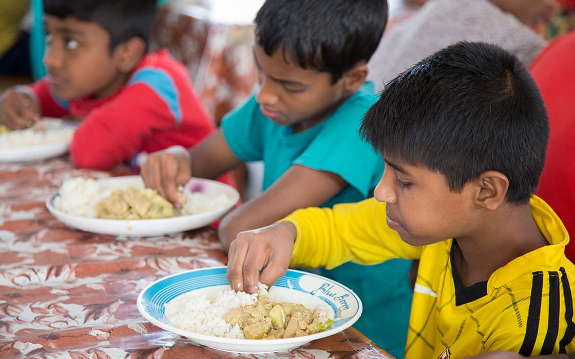 Drei Jungen sitzen an einem Tisch, essen Reis und Curry von Tellern und konzentrieren sich auf ihr Essen.
