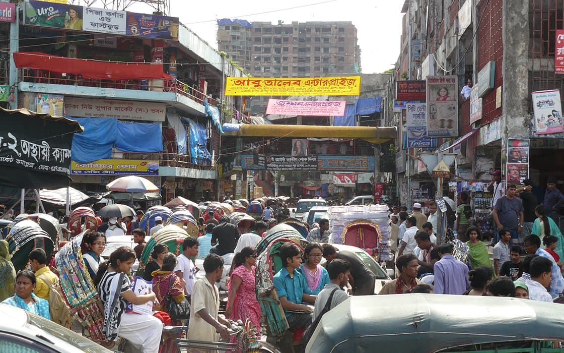 Eine geschäftige Straßenmarktszene in einem städtischen Gebiet mit Menschenmassen, Rikschas, Geschäften und bunten Schildern.