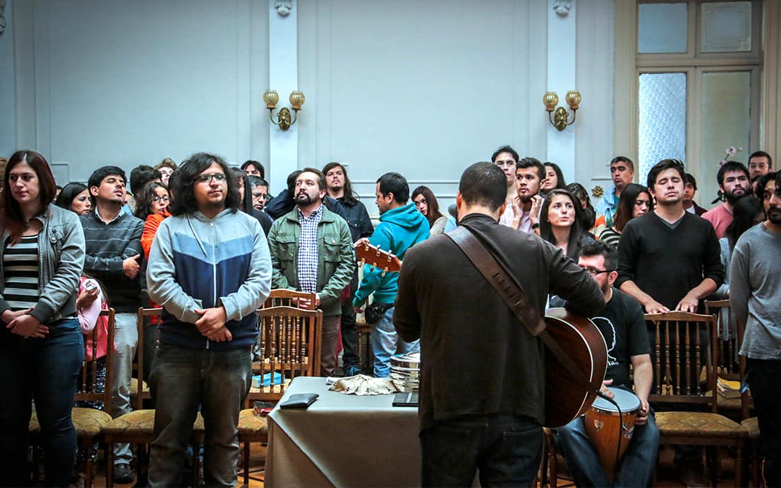 Eine Gruppe von Menschen steht in einem Raum und singt gemeinsam, während zwei Musiker vorne im Raum Gitarre spielen.