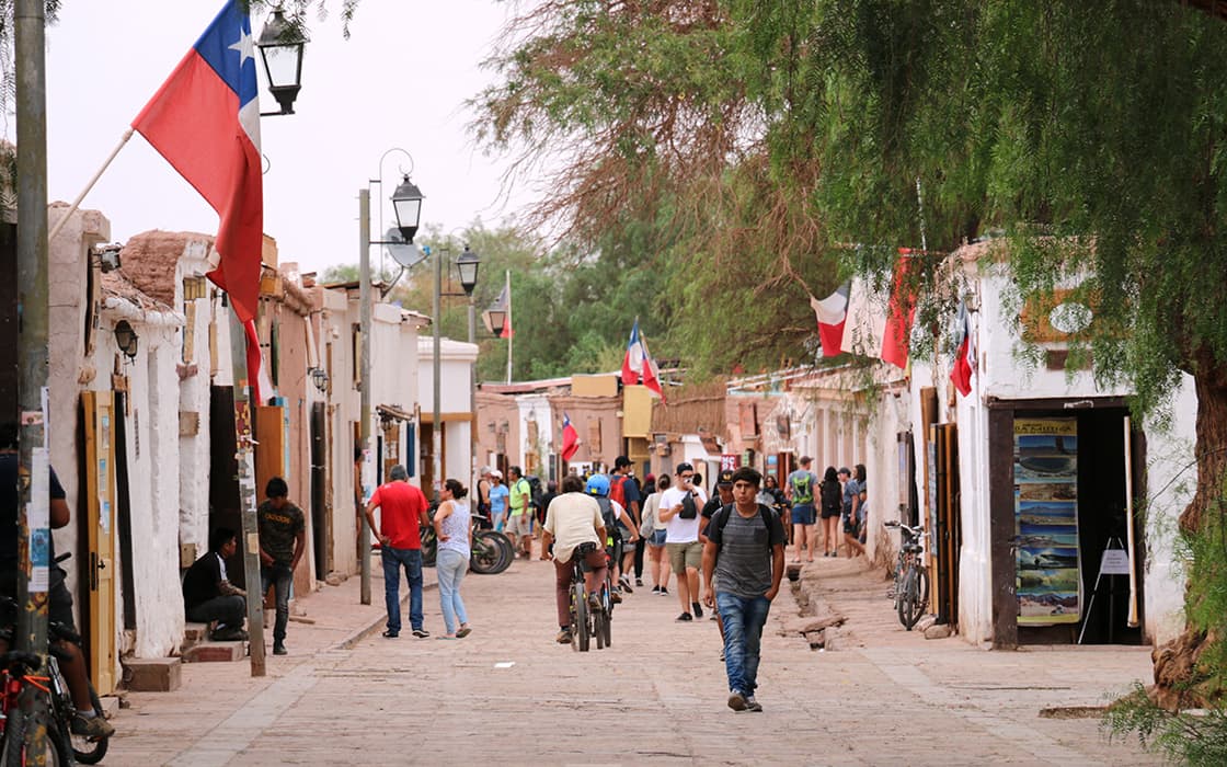 Die Menschen spazieren und fahren mit dem Fahrrad entlang einer rustikalen, mit Fahnen und Bäumen gesäumten Straße in einer lebendigen Stadt.