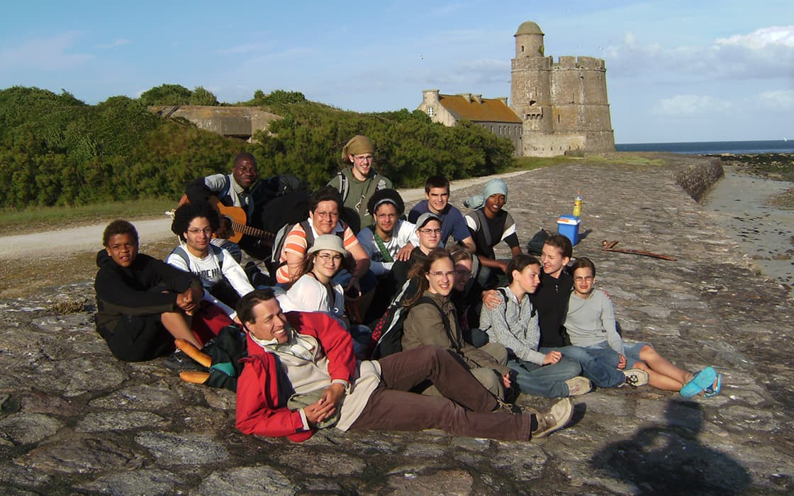 Eine Gruppe von Menschen sitzt und posiert zusammen auf einem Steinweg in der Nähe eines historischen Steinforts am Meer.