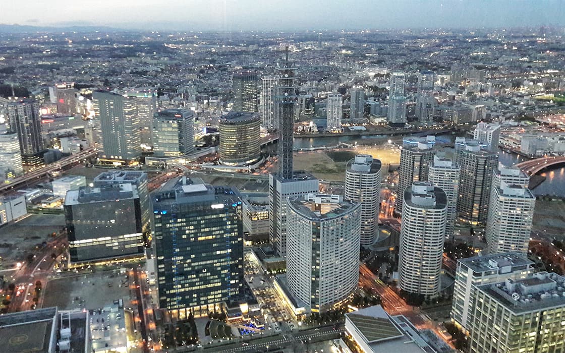 Luftaufnahme einer modernen Stadt mit hohen Gebäuden, Flüssen und entfernten Bergen in der Abenddämmerung.