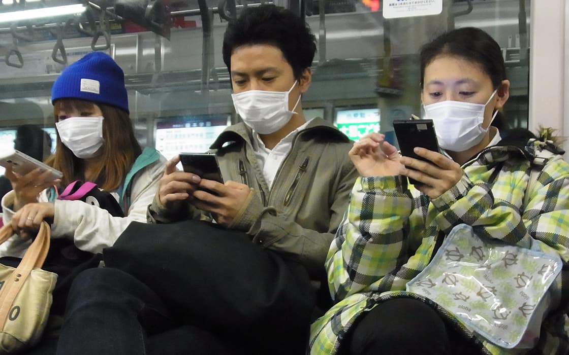 Drei maskierte Personen sitzen in einem Zug und schauen jeweils auf ihr Smartphone.