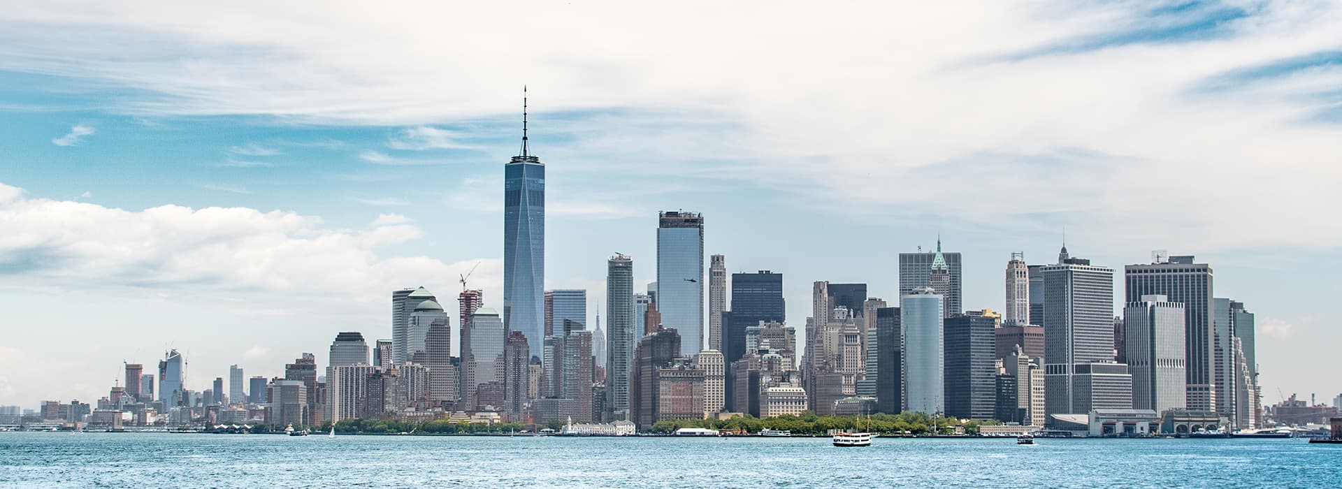 Skyline von New York City mit hohen Wolkenkratzern bei teilweise bewölktem Himmel, von der anderen Seite des Wassers aus gesehen.