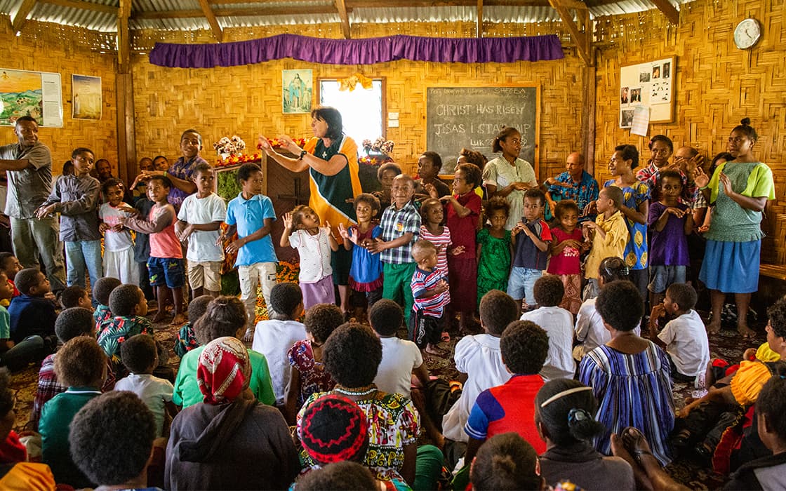 Eine Gruppe von Kindern und Erwachsenen versammelt sich in einer farbenfrohen Kirche in Papua-Neuguinea, um gemeinsam zu singen oder einer Aktivität nachzugehen.