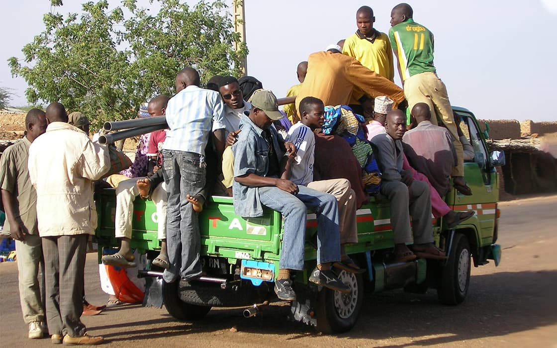 Eine Gruppe von Menschen drängt sich an einem sonnigen Tag auf der Ladefläche eines grünen Pickups.