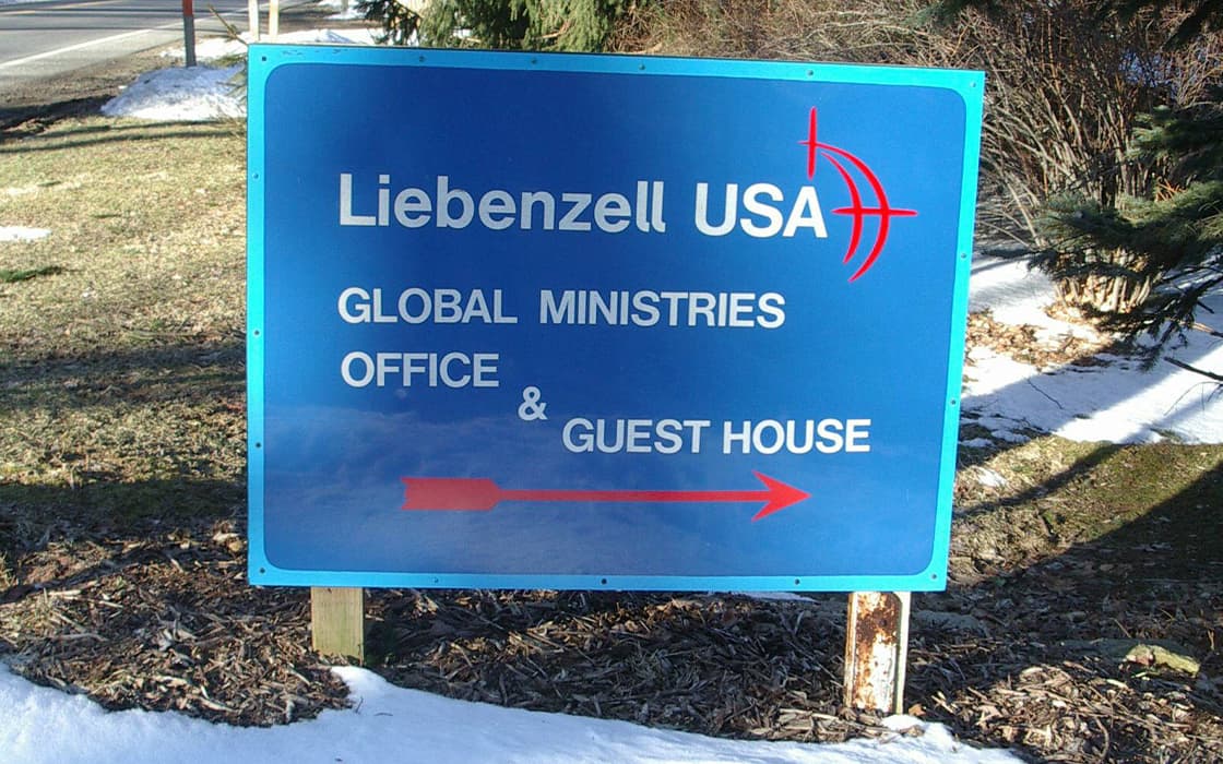 Auf dem blauen Schild steht: Liebenzell USA Global Ministries Office & Guest House mit einem roten Pfeil, der nach rechts zeigt.