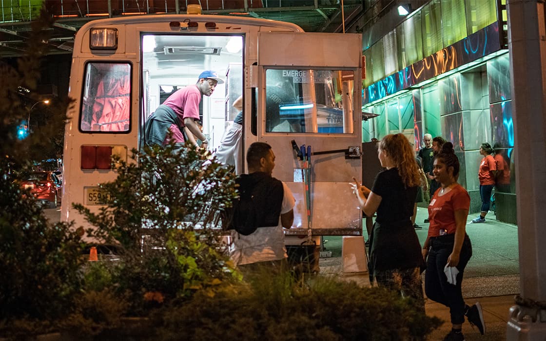 Menschen versammeln sich und bestellen Essen an einem hell erleuchteten Imbisswagen, der nachts auf einer Straße in der Stadt steht.