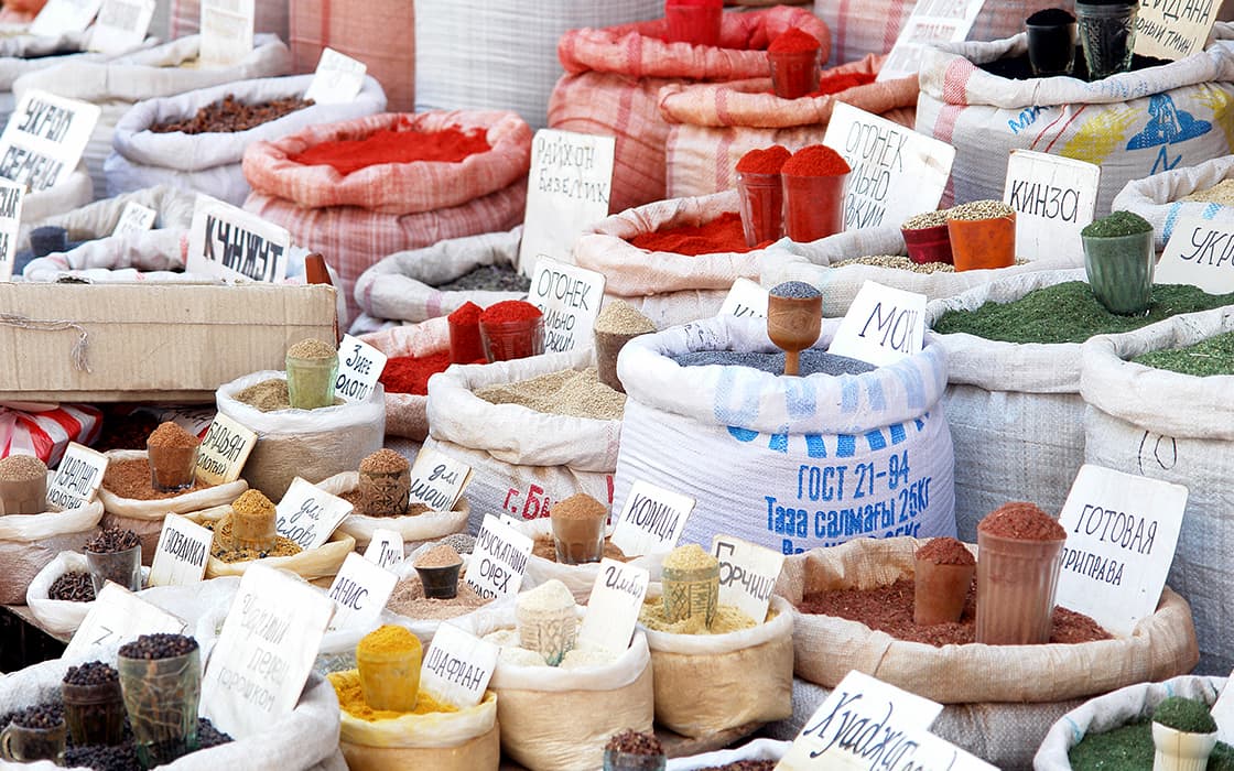 An einem Marktstand stehen Säcke mit bunten Gewürzen und Kräutern mit handgeschriebenen Etiketten in russischer Sprache.