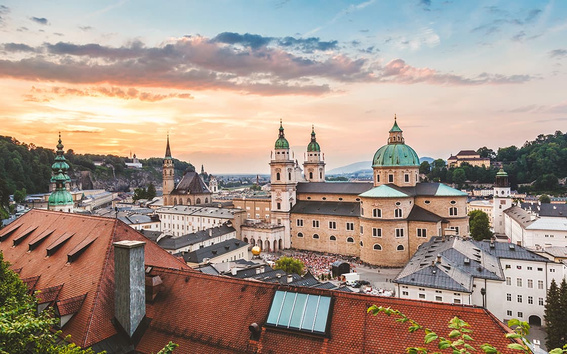 Ein Panoramablick auf Salzburg, Österreich, mit historischen Gebäuden und Kirchenkuppeln bei Sonnenuntergang unter einem leuchtenden Abendhimmel.