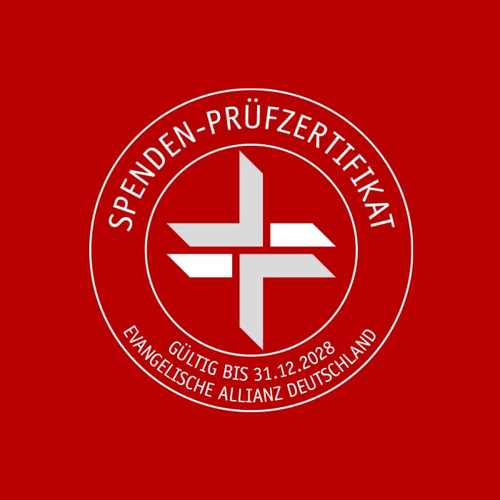 Rot-weiße runde Zertifizierungsplakette mit deutschem Text, einem geometrischen Kreuz und dem Schriftzug "Jetzt spenden.
