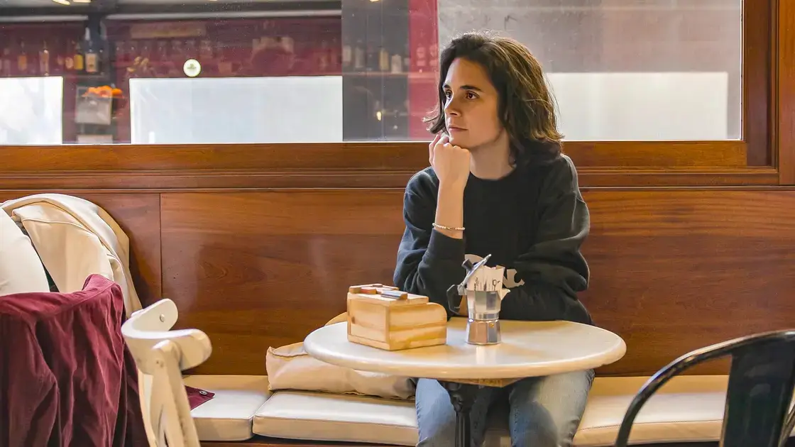 Eine Person sitzt allein an einem Kaffeetisch und blickt in Einsamkeit aus dem Fenster, das Kinn auf die Hand gestützt.