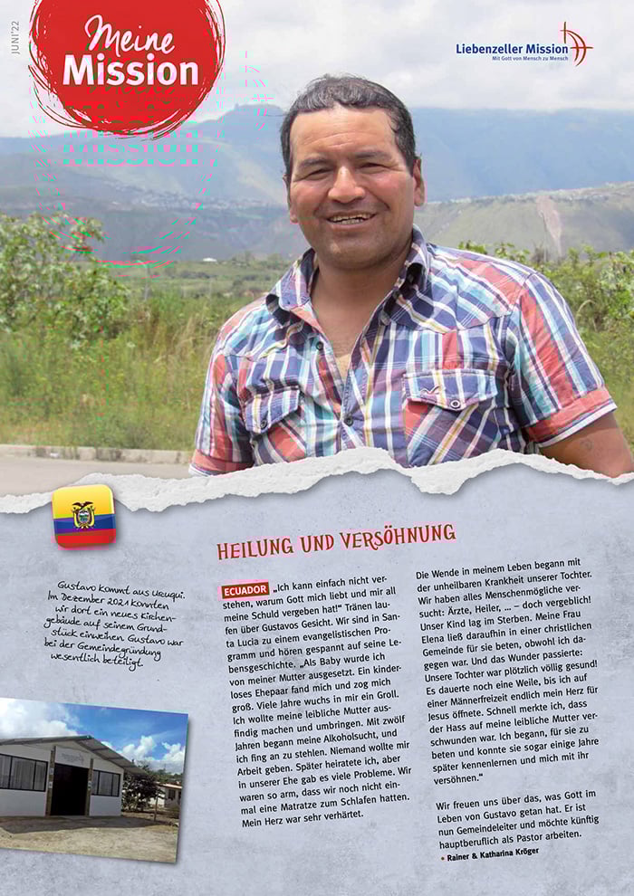 Ein lächelnder Mann im karierten Hemd steht im Freien auf der Mission Juni 2022, mit Bergen und Grün unter einem blauen Himmel.